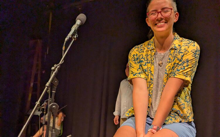 person sitting on stool next to microphone smiling