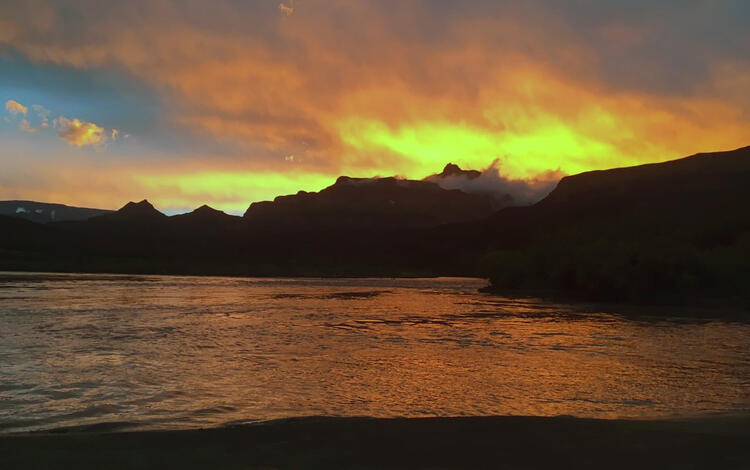 An orange, yellow and blue sunset reflects orange light on the Colorado River