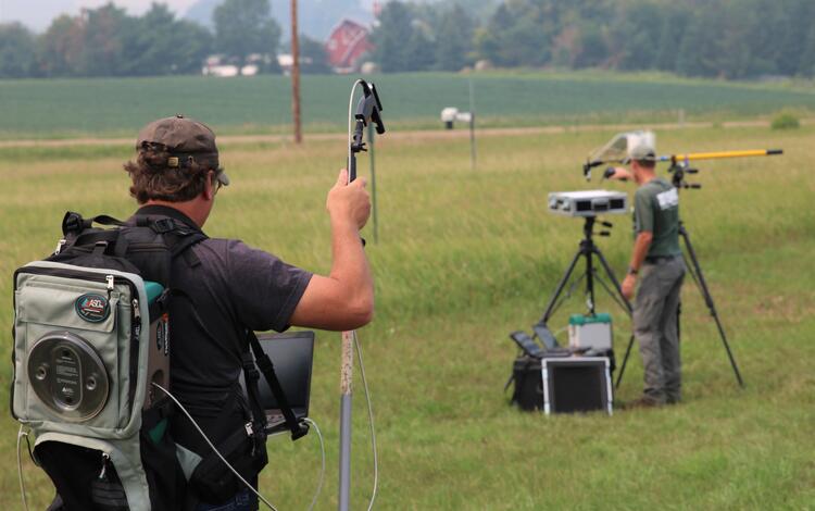 Two men use equipment in a grassy area
