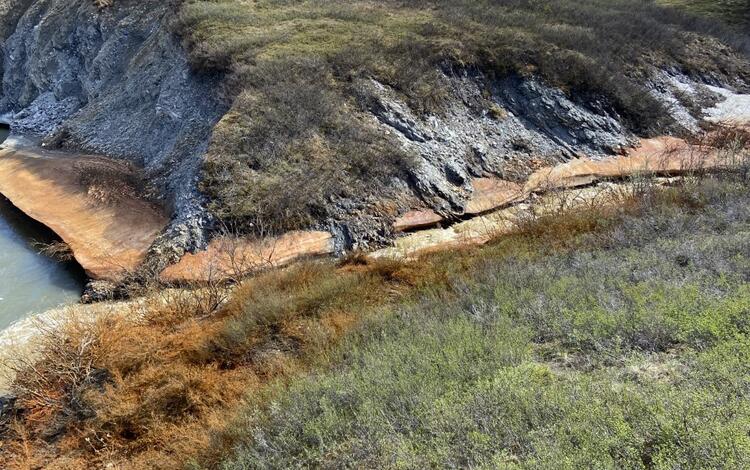 Hills with patches of snow and orange coloring along the bank and vegetation along the tributary of the Agashashok River, AK