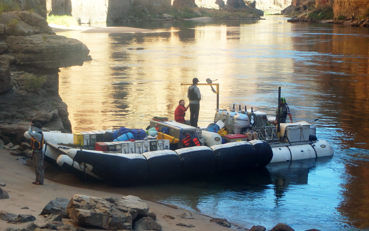 Researchers stand on a boat that's parked on a sandbar along the Colorado River in Grand Canyon