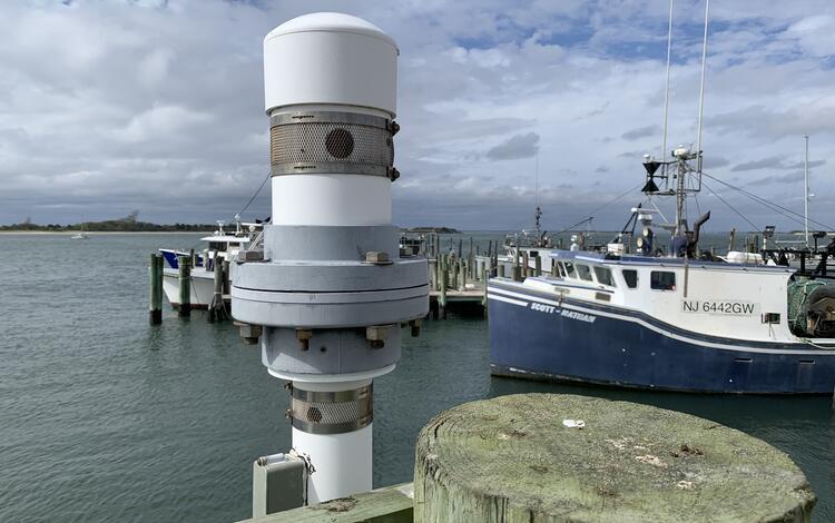 A white and grey cylindrical object with screened ventholes in its side sits atop a tube that reaches down into the bay below