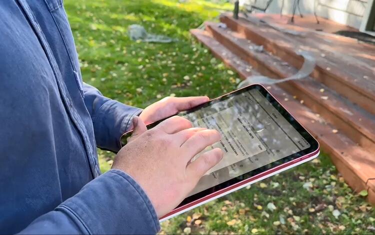 someone wearing a blue shirt holds a tablet at the steps of a house