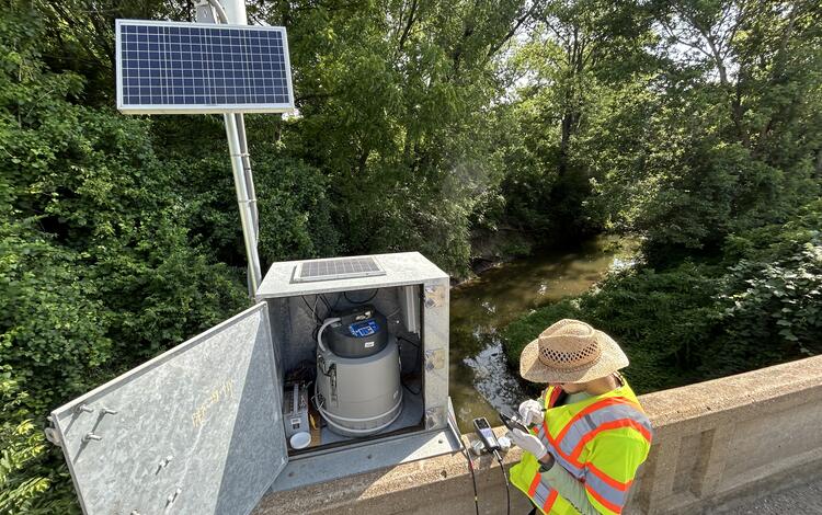 Scientist collecting field parameters and checking the autosampler at streamgage on bridge