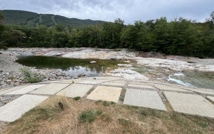Low lying water in a river with a ski resort in the background during the summer.