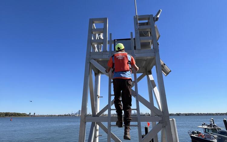 Technician climbing an aluminum tower housing the tide sensors 