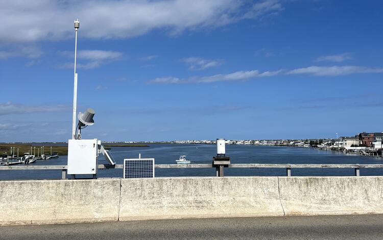 Looking at a box housing a weather sensor and mast and a rain gage next to it as we look out over the bay