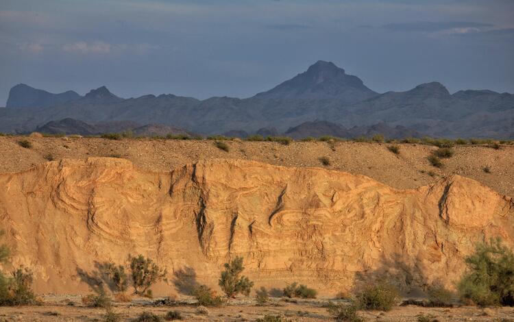 An illuminated steep bluff face in the desert that reveals complexly deformed and folded sedimentary strata.