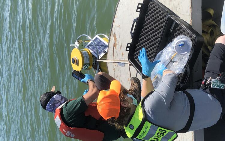 Scientists checking a water buoy from the bow of a boat